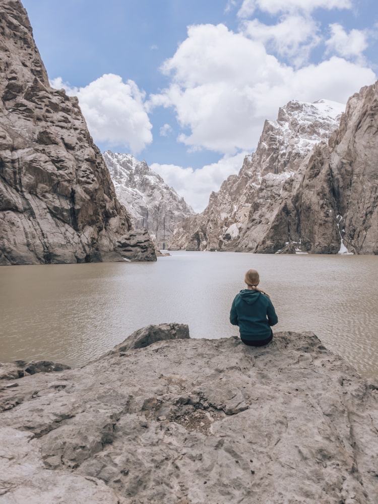 A girl sitting on a rock and admiring Kel-Suu Lake and the surrounding mountains in Kyrgyzstan